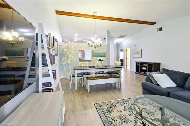 Living area with a chandelier, vaulted ceiling with beams, and wood finished floors
