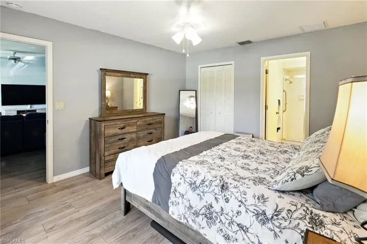 Bedroom with a closet, baseboards, ensuite bathroom, visible vents, and wood finished floors