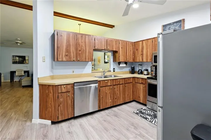 Kitchen featuring a sink, stainless steel appliances, a ceiling fan, and vaulted ceiling with beams