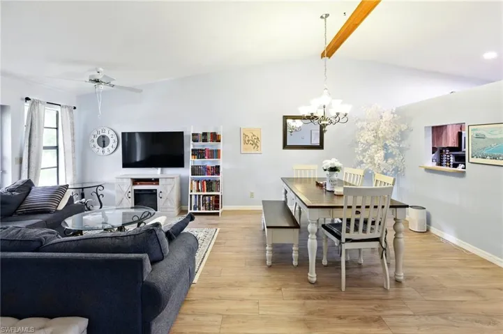 Dining space with baseboards, lofted ceiling with beams, light wood-type flooring, and ceiling fan with notable chandelier