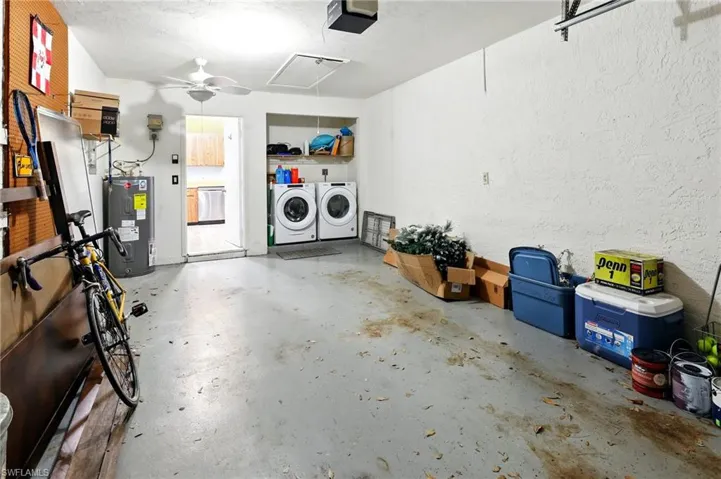 Garage with washing machine and clothes dryer, a ceiling fan, electric water heater, and a garage door opener