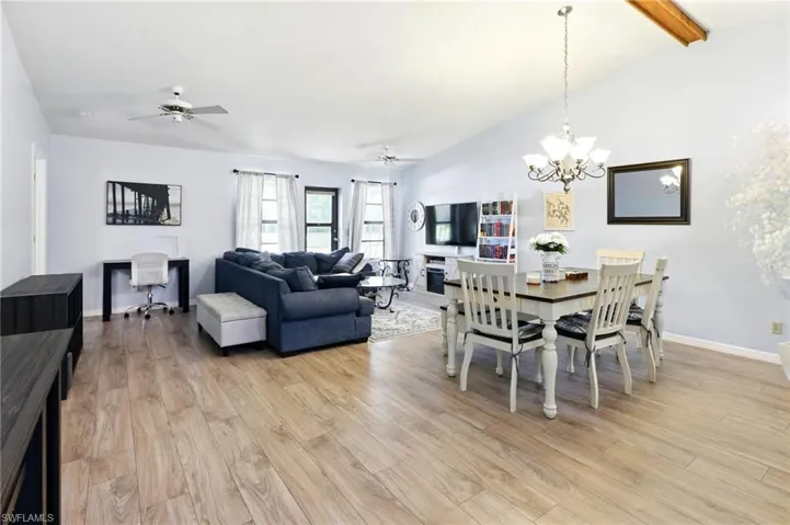 Dining area with baseboards, lofted ceiling with beams, light wood-type flooring, and ceiling fan with notable chandelier