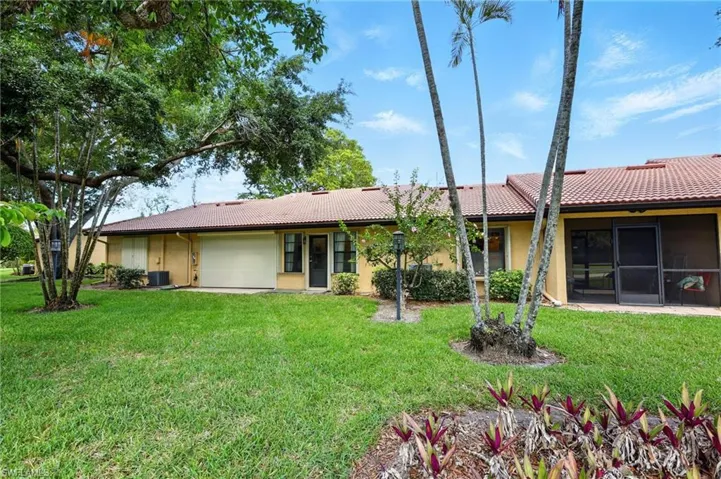 View of back of property featuring stucco siding, a garage, a tiled roof, and a front lawn