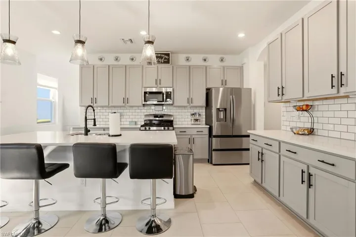 Kitchen with stainless steel appliances, a kitchen bar, hanging light fixtures, light stone counters, and an island with sink