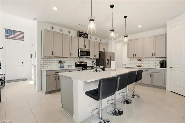 Kitchen with gray cabinetry, a kitchen bar, decorative light fixtures, a center island with sink, and stainless steel appliances