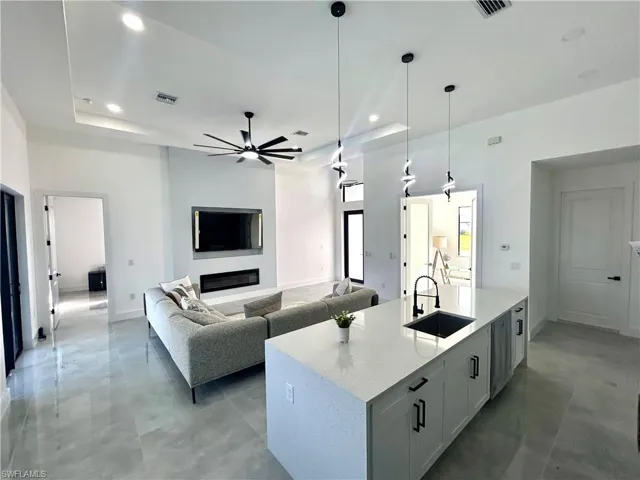 Kitchen with sink, an island with sink, decorative light fixtures, light stone counters, and white cabinetry