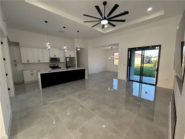 Kitchen featuring stainless steel appliances, a raised ceiling, a center island with sink, white cabinetry, and hanging light fixtures