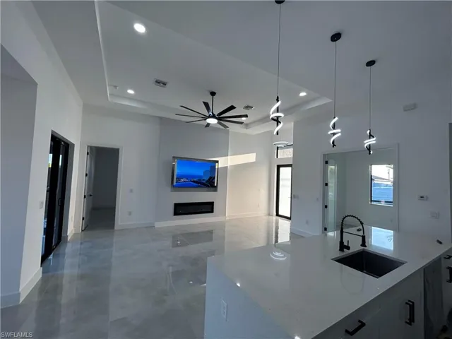 Kitchen featuring a raised ceiling, light stone counters, sink, and decorative light fixtures