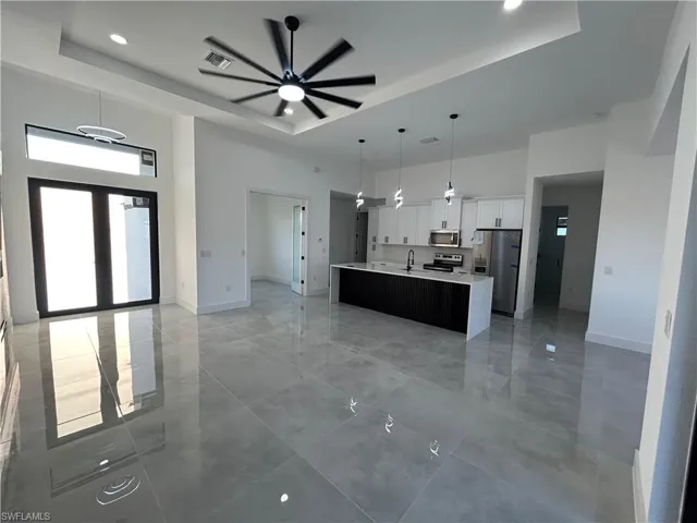 Kitchen featuring ceiling fan, stainless steel appliances, decorative light fixtures, a kitchen island with sink, and white cabinets