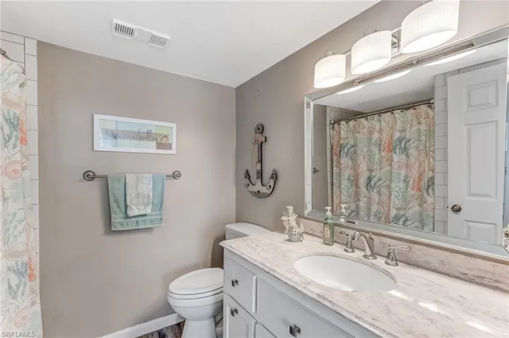 Elegant bathroom with a sleek single vanity, pristine white cabinetry, a custom-designed mirror, and a spacious walk-in shower.