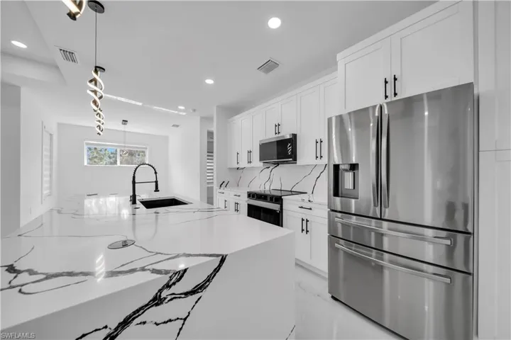 Kitchen featuring stainless steel appliances, hanging light fixtures, light stone counters, white cabinetry, and backsplash