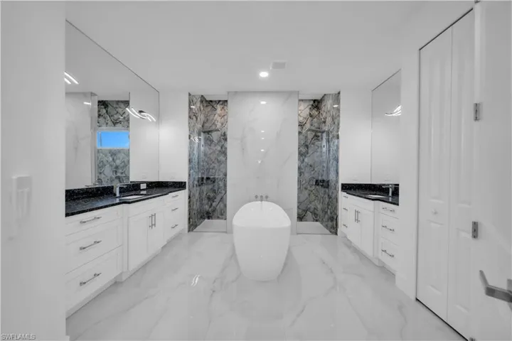 Bathroom featuring a marble finish shower, two vanities, a freestanding bath, stone wall, and recessed lighting
