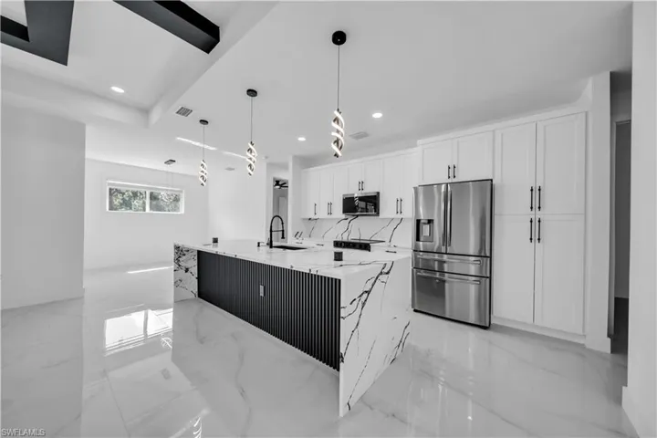 Kitchen with stainless steel appliances, a kitchen island with sink, pendant lighting, light stone countertops, and white cabinets