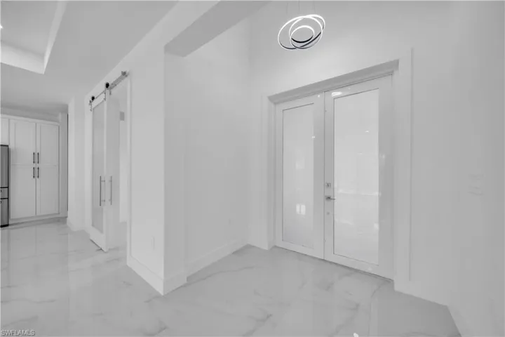 Foyer entrance with a barn door, light marble finish floors, and french doors