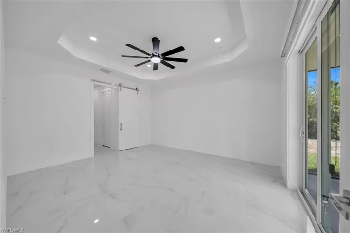 Unfurnished room featuring a ceiling fan, a barn door, recessed lighting, and light marble finish flooring