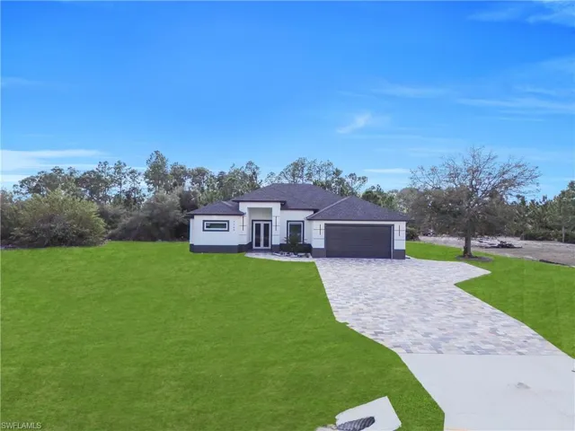 View of front of home with decorative driveway, a front yard, an attached garage, stucco siding, and a shingled roof