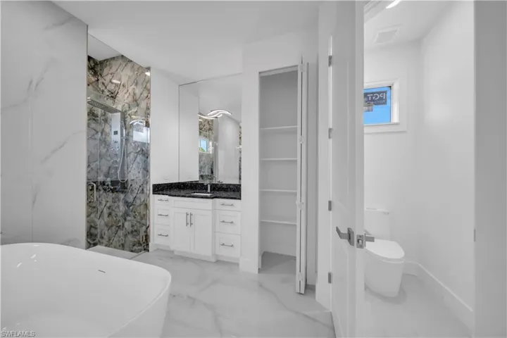 Bathroom with a marble finish shower, a freestanding bath, vanity, light marble finish floors, and a walk in closet