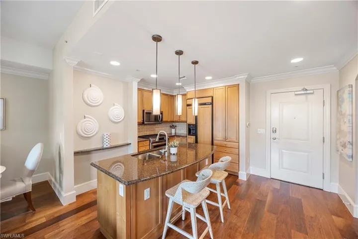 Kitchen featuring sink, crown molding, hanging light fixtures, paneled built in fridge, and dark stone counters