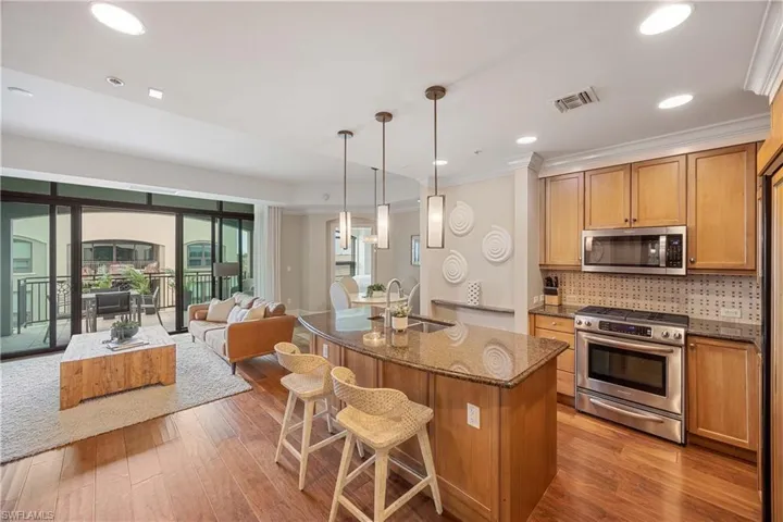 Kitchen featuring stone counters, pendant lighting, sink, stainless steel appliances, and a center island with sink