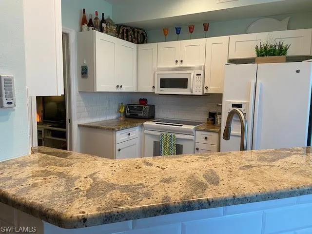 Kitchen with white appliances, white cabinetry, and backsplash