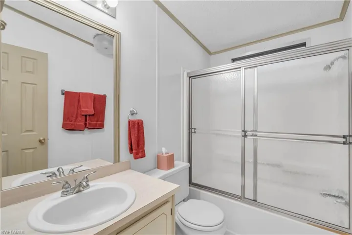 Full bathroom featuring shower / bath combination with glass door, a textured ceiling, toilet, vanity, and ornamental molding