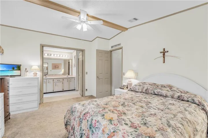 Bedroom with lofted ceiling with beams, light carpet, ceiling fan, and connected bathroom
