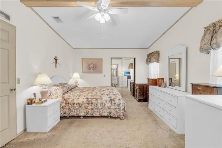 Carpeted bedroom with a closet, ceiling fan, and vaulted ceiling with beams