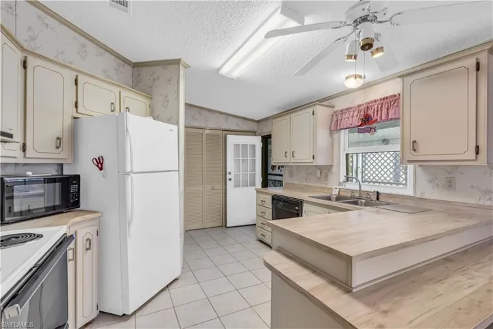 Kitchen featuring a textured ceiling, ceiling fan, black appliances, vaulted ceiling, and sink