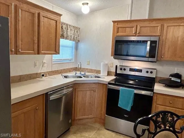 Kitchen featuring stainless steel appliances, brown cabinetry, light countertops, a textured ceiling, and light tile patterned floors