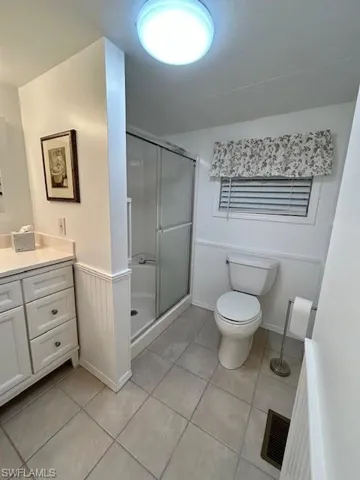 Bathroom featuring a stall shower, light tile patterned floors, vanity, and wainscoting