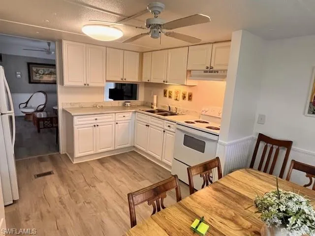 Kitchen featuring white appliances, light countertops, white cabinetry, light wood finished floors, and a ceiling fan
