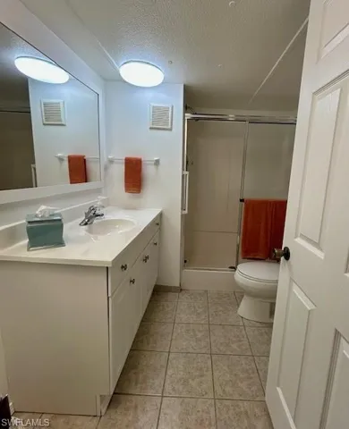 Full bath with vanity, a textured ceiling, a stall shower, and light tile patterned flooring