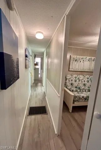 Hall featuring light wood-style flooring, crown molding, and a textured ceiling