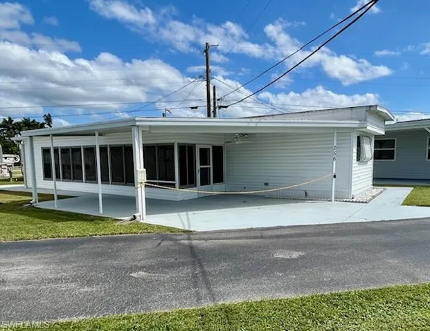 Rear view of property with an attached carport, concrete driveway, a sunroom, and a yard
