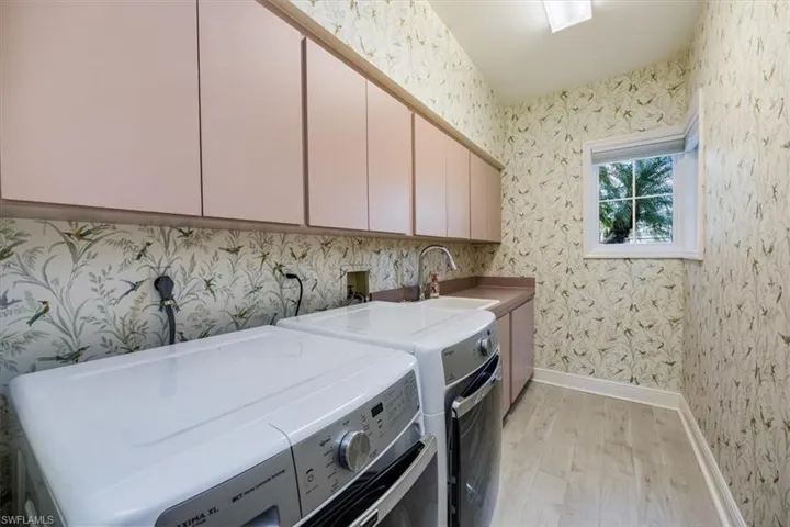 Laundry area with sink, washer and clothes dryer, light wood-type flooring, and cabinets