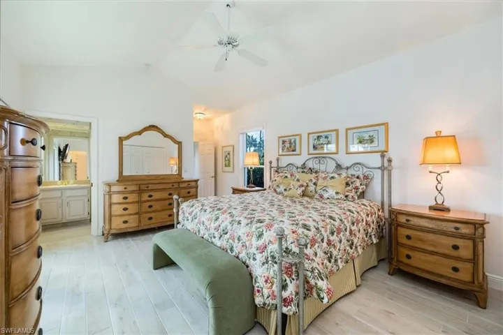 Bedroom featuring ceiling fan, vaulted ceiling, light hardwood / wood-style floors, and ensuite bathroom