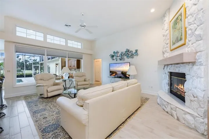 Living room with a towering ceiling, a fireplace, light wood-type flooring, and ceiling fan