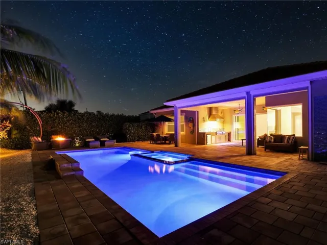 Pool at night featuring outdoor lounge area, an in ground hot tub, and a patio