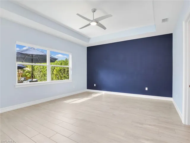Empty room with light hardwood / wood-style floors, ceiling fan, and a tray ceiling