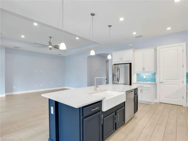 Kitchen featuring sink, decorative light fixtures, a center island with sink, white cabinets, and appliances with stainless steel finishes