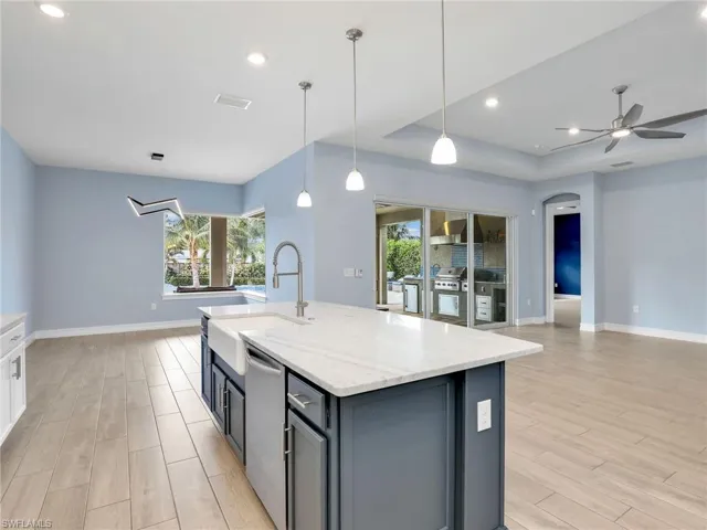 Kitchen with light wood-type flooring, decorative light fixtures, light stone counters, and a center island with sink