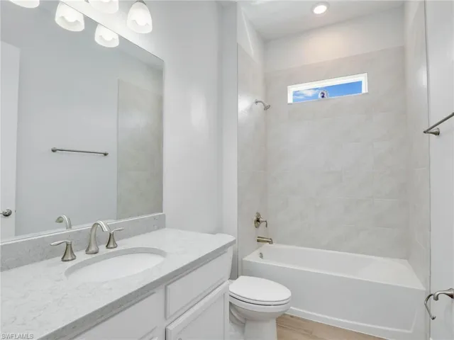 Full bathroom with vanity, toilet, wood-type flooring, and tiled shower / bath