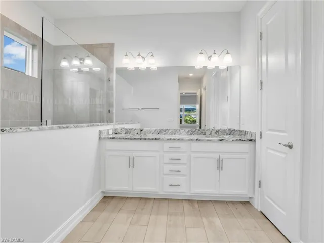 Bathroom featuring a wealth of natural light, vanity, wood-type flooring, and tiled shower