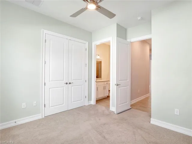 Unfurnished bedroom with light carpet, a closet, ensuite bath, and ceiling fan