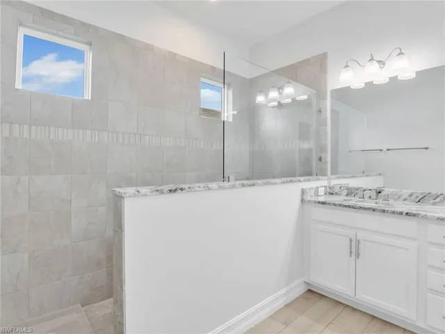 Bathroom featuring a tile shower, vanity, and a healthy amount of sunlight