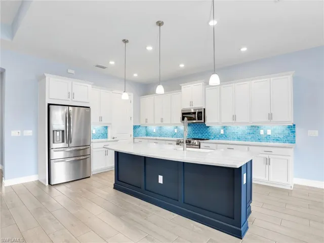 Kitchen featuring appliances with stainless steel finishes, decorative light fixtures, white cabinetry, and an island with sink