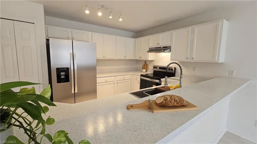 Kitchen featuring stainless steel appliances, white cabinetry, light stone countertops, and track lighting