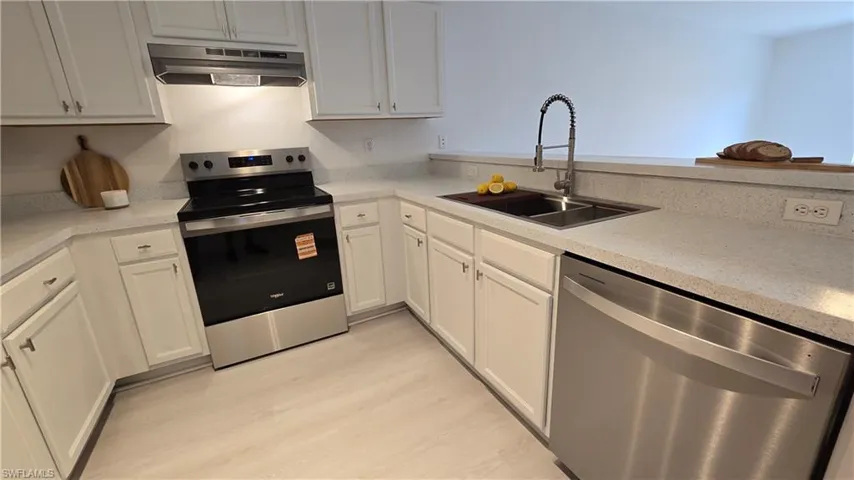 Kitchen with stainless steel appliances, white cabinetry, light wood-style flooring, and light stone countertops