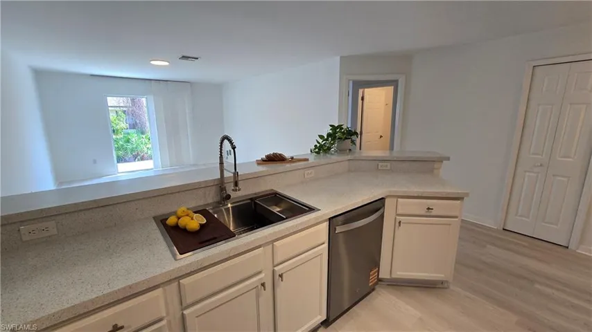 Kitchen with dishwasher, light wood finished floors, light stone counters, and white cabinetry