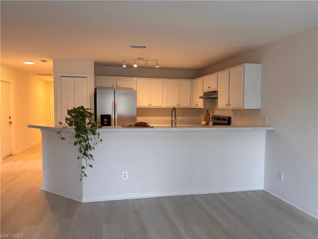 Kitchen with light countertops, stainless steel appliances, a peninsula, white cabinets, and light wood-type flooring